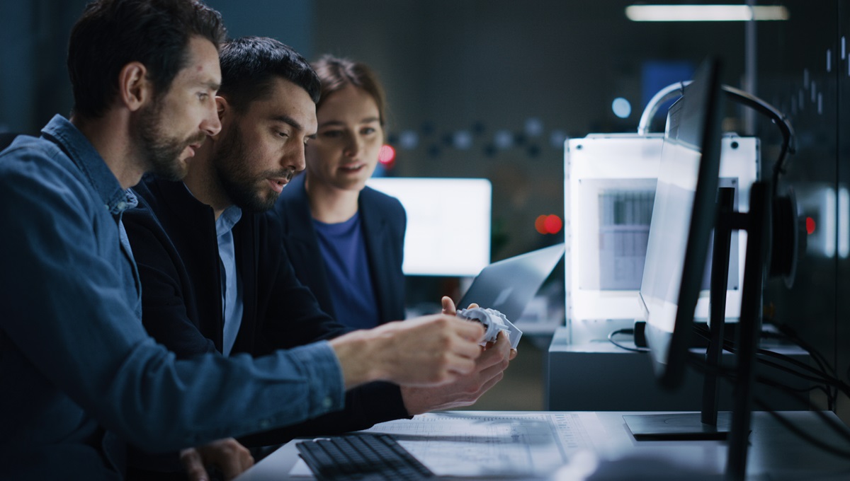 Corporate photo of three colleagues examining a machine part in an office by the Fullframe Creative agency.